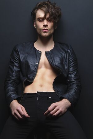 Muscle strong beautiful stripped male model in denim jeans and leather jacket on black isolated font...
