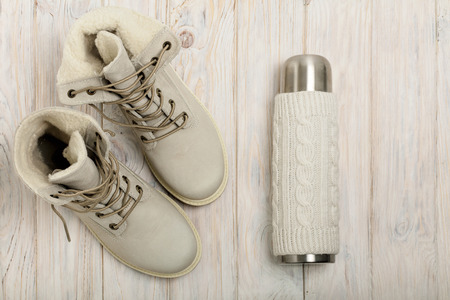 Winter light boots and a bottle in the knitted cover on the bright wooden background.