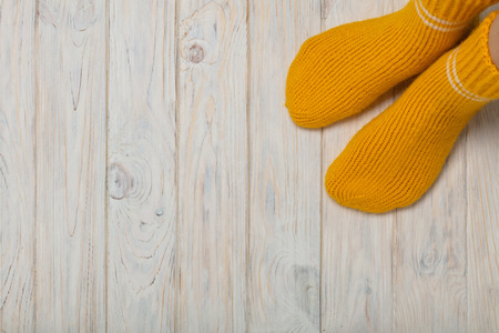 Female feet in knitted yellow socks on white wooden background.