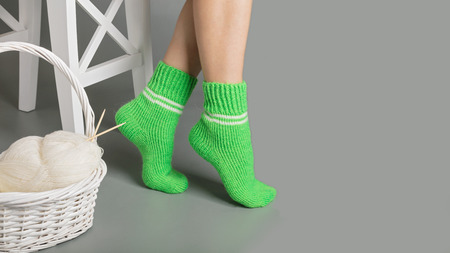 Female legs in green knitted socks near the basket with yarn and knitting.の写真素材