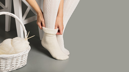 Female feet in white knitted stockings and socks near the basket with yarn and knitting.の写真素材