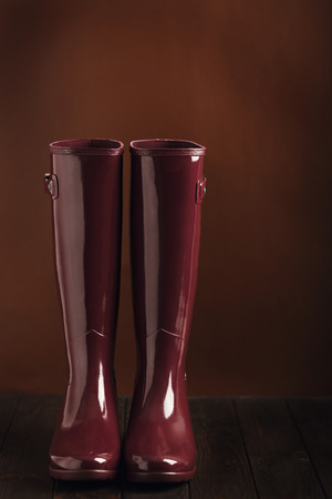 Photo in low key. Rubber boots burgundy color on a brown background. Selective focus.の写真素材