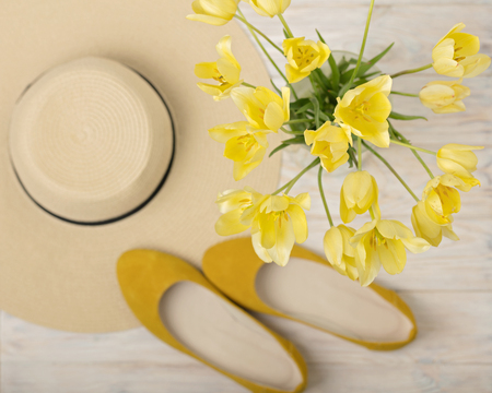 Yellow women's shoes (flats), hat and yellow tulips on a light wooden background. Selective focus.の写真素材