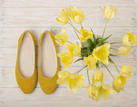 Yellow women's shoes (flats) and yellow tulips on a light wooden background. Selective focus.の写真素材