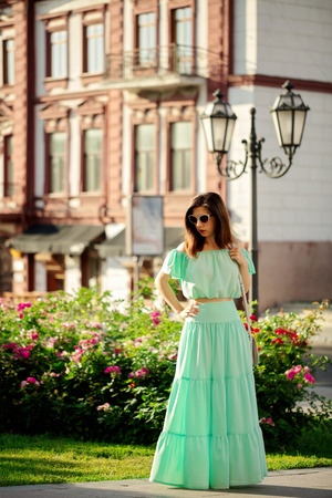 Young beautiful woman in a light green pastel long dress is walking along the street in the city in the summer. Selective focus.の写真素材