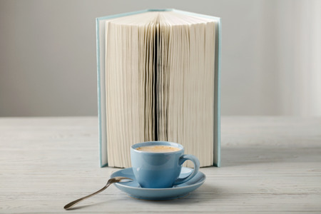 Coffee in a light blue cup and book in blue cover on a wooden background. Selective focus.の写真素材