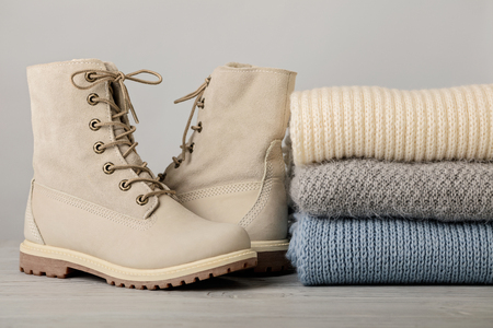 Leather women's light winter boots and a pile of knitted things (sweaters, scarves, gloves). Selective focus.の写真素材