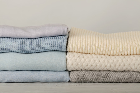 Pile of knitted clothes (sweaters, scarves, pullovers) blue, white and grey colors. Selective focus.の写真素材