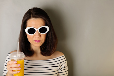 Woman in a white striped top and white sunglasses drinks orange juice. Selective focus.の写真素材