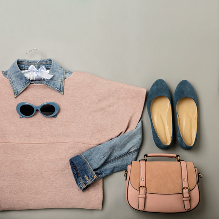 Flat lay of a casual woman fashion outfit - jeans, pink dress, handbag and sunglsses. Top view on gray background. Selective focus.の写真素材