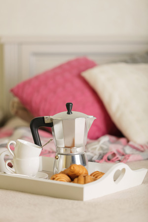 Breakfast in bed. On a white wicker tray there is a coffee maker, coffee cups and croissants. Selective focus.の写真素材