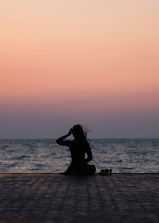 Silhouette of a girl on a sunset background (sunrise) on the sea, horizon line. Summer walk on the beach.の写真素材