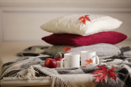 Home comfort and warmth in the autumn time. Gray plaid, knitted pillows, tea and autumn red maple leaves. Selective focus.の写真素材
