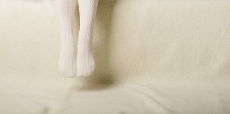 Female legs in warm white knitted tights on a white background made of faux furの写真素材