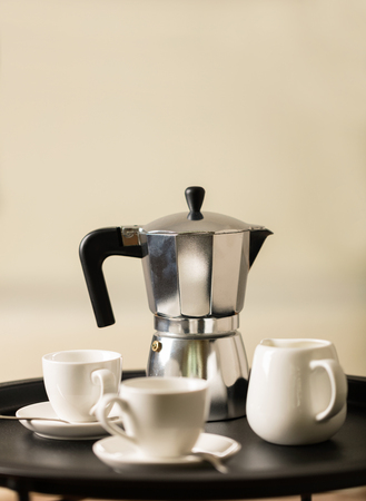 Round black metal coffee table with a coffee maker and a cup on the background of a white sofa with a gray blanket. Selective focus.の写真素材