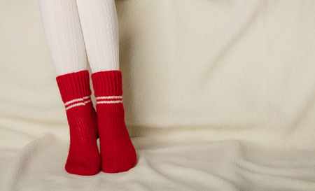 Female legs in warm white knitted tights and red socks on a white background made of faux furの写真素材