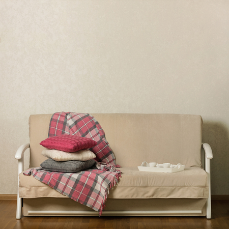 Beige sofa with plaid and colorful pillows (pink, grey, white) and tray with cups of coffee in the living room. Selective focus.の写真素材