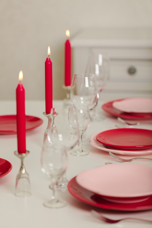 Merry Christmas and Happy New Year! Table setting - red and pink dishes, holiday knitted decor - Santa Claus knitted hats on the bottle with wine, red candles. Selective focus.の写真素材