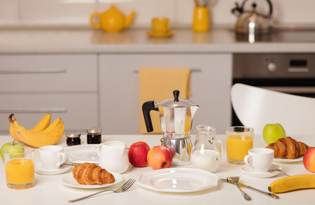 Breakfast time. Croissants and orange juice, jam and honey. Coffee with cream or milk. Fruits - bananas, red and green apples.  Breakfast on a white table.の写真素材