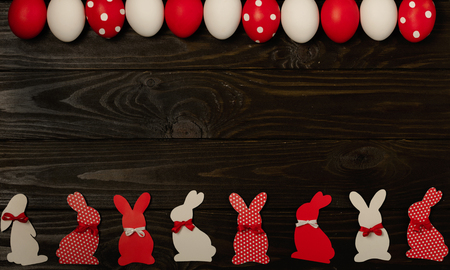 Happy Easter! Painted Easter eggs and Easter decoration - Easter bunnies with ribbons - red, white and red with white polka dots on a brown wooden background. Selective focus.の写真素材