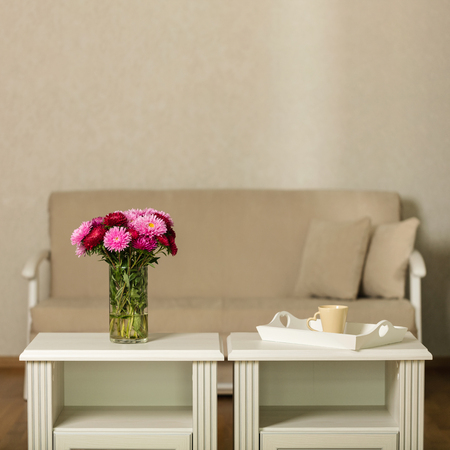 Beige sofa with pillows in the living room and vase with Flowers (Michaelmas daisy, asters). Selective focus.の写真素材