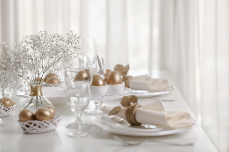 Happy Easter! Golden decor and table setting of the Easter table with white dishes of white color....