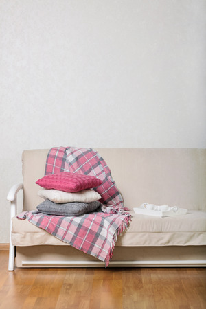 Beige sofa with plaid and colorful pillows (pink, grey, white) and tray with cups of coffee in the living room. Selective focus.の写真素材