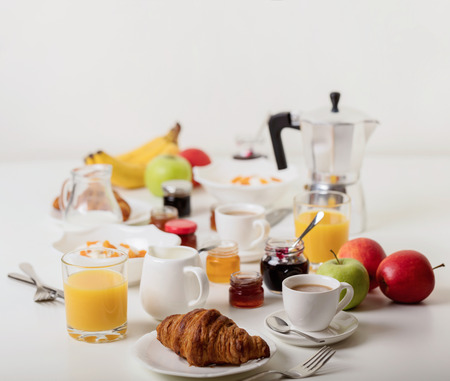 Breakfast time. Croissants and orange juice, jam and honey. Coffee with cream or milk. Fruits - bananas, red and green apples. Ricotta with sour cream, nuts and dried apricots. Breakfast on a white table.の写真素材