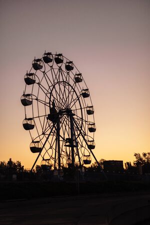 Silhouette of a ferris wheel at sunrise (sunset) of the sun on a background of trees and grass. Beautiful background with copy space.の写真素材
