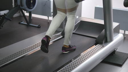 Female legs walking and running on treadmill in gym. Young woman exercising during cardio workout....