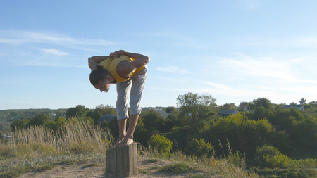 Young sporty man standing at yoga pose outdoor. Caucasian guy practicing yoga moves and positions in nature. Athlete balancing on one leg. Beautiful landscape as background. Healthy active lifestyleの写真素材