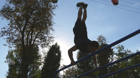 Strong muscular man doing a handstand in a park. Fit muscular male fitness guy doing stunts on...
