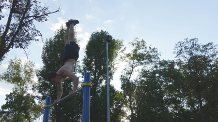 Strong muscular man doing a handstand in a park. Fit muscular male fitness guy doing stunts on...
