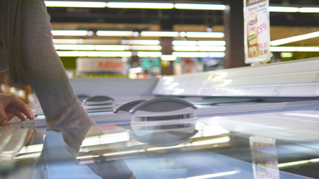 Female hands opening glass door in the refrigerated section at the supermarket and choosing ice cream. Young woman taking product from fridge in shop and putting it into the basket. Close upの写真素材