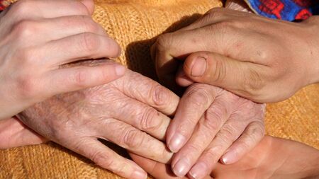 A young mans and womans hands comforting a old pair of hands of grandmother outdoor.
