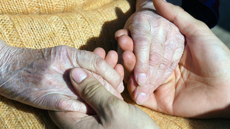 A young male hands comforting an elderly pair of hands of grandma outdoor close up.