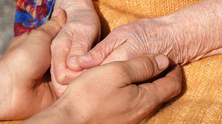 A young dirty working male hands comforting an elderly pair of hands of grandmother outdoor close up.の写真素材