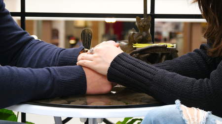 Happy couple holding and touching each others hands at cafe in shopping mall. Male hands are stroking the female hand tenderlyの写真素材