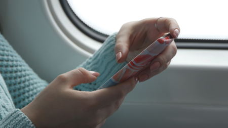 Young woman traveling in a train and using mobile phone. Female hand sends a message from the smartphone. Arm of girl chatting with friends. Close upの写真素材