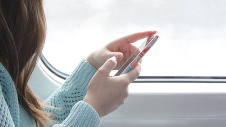 Young woman traveling in a train and using mobile phone. Female hand sends a message from the...