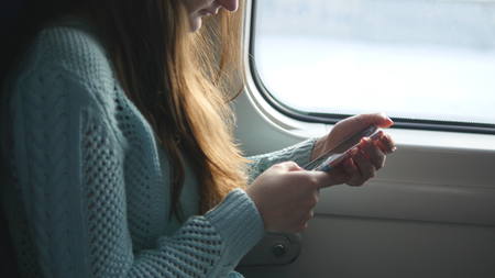 Young girl travelling in a train and using mobile phone. Beautiful woman sends a message from the smartphone. Attractive girl chatting with friendsの写真素材
