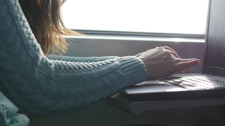 Female hands typing on keyboard of laptop in train. Woman chatting with friends during traveling on railway. Young girl using notebook. Arm print a message. Close upの写真素材