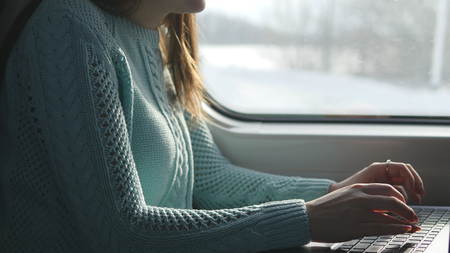 Female hands typing on keyboard of laptop in train. Woman chatting with friends during traveling on...
