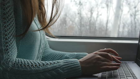 Female hands typing on keyboard of laptop in train. Woman chatting with friends during traveling on...