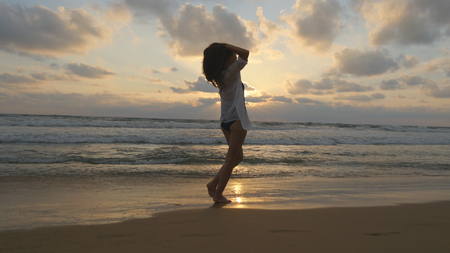 Happy woman walking and spinning on the beach near the ocean. Young beautiful girl enjoying life and having fun at sea shore. Summer vacation or holiday. Sunset landscape at background Close upの写真素材