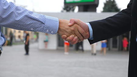 Business handshake with blurred city background. Two businessmen greeting each other in urban...