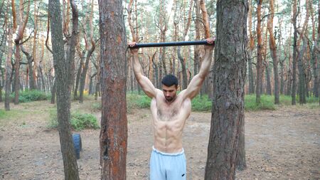 Strong man showing some exercises on horizontal bar. Muscular guy doing pull ups. Athlete performs...