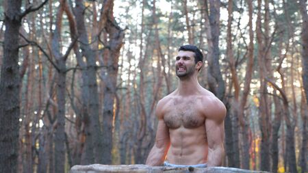 Muscular man lifting hard weight training biceps. Strong and hardy guy working out outdoor at sunset background. Athlete with naked torso exercising in nature. Concept of sport lifestyle. Dolly shotの写真素材