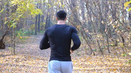 Unrecognizable man running along forest path. Male sportsman working out at nature. Strong and...