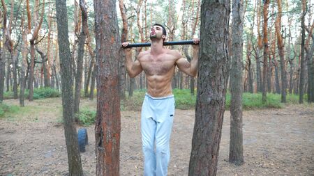 Athletic man showing some abdominal exercises on horizontal bar. Muscular guy working out at forest....